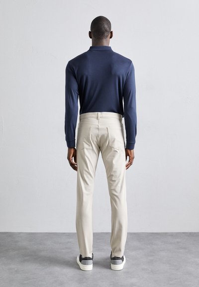 Marineblaues Langarm-Polohemd, beigefarbene Hose mit Gesäßtaschen und graue Sneakers. Glatte Textur, lässige Passform und neutrale Farben.