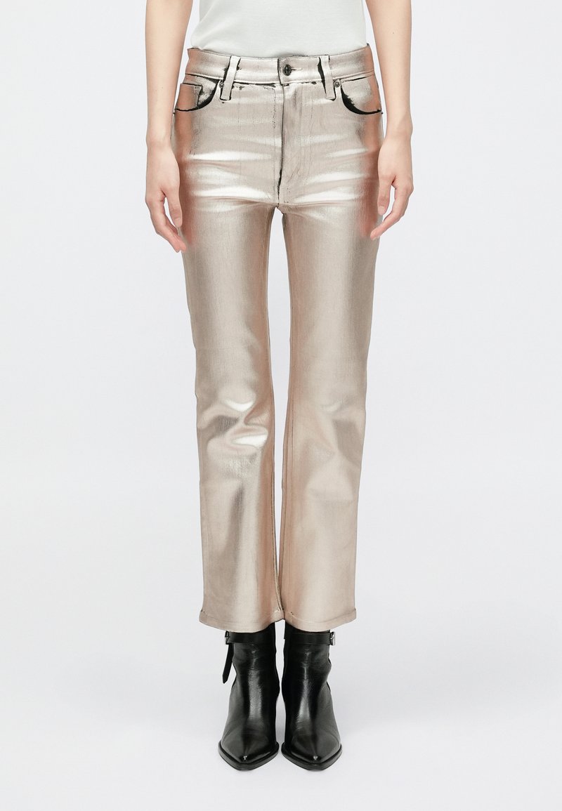 Pantalons dorés métalliques avec une coupe droite, un style à cinq poches et des coutures contrastées. Assortis à des bottines noires à la cheville.