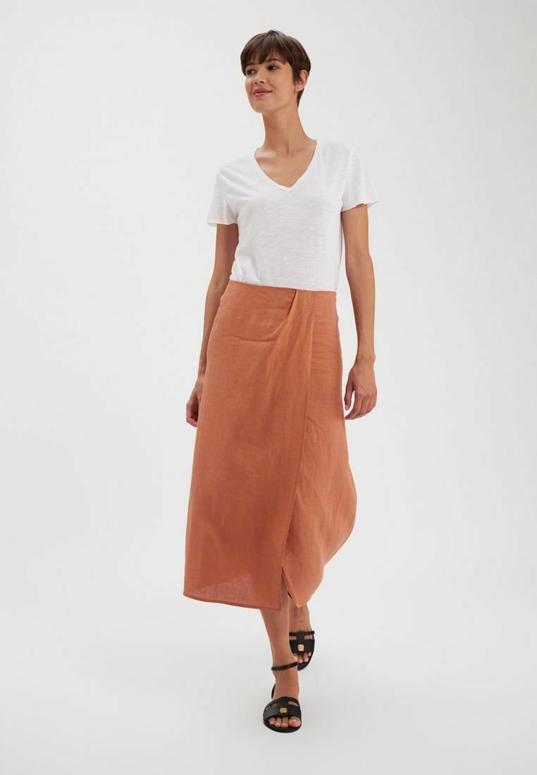 Jupe en lin rouille avec un design croisé à l'avant, associée à un t-shirt blanc uni à col en V et des sandales noires à lanières.