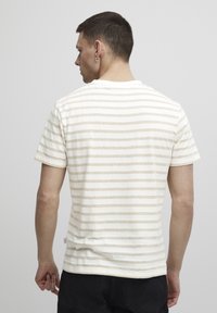 Stripet t-skjorte i krem og beige, med korte ermer, rund halslinning og en myk bomullstekstur. Merke synlig på siden.