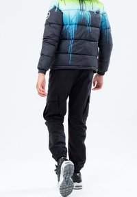 Zwarte pufferjack met een gradient ontwerp in blauw en groen, gecombineerd met zwarte cargobroek en sneakers met een witte zool.