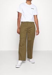 Olivově zelené kalhoty s rovného střihu, bavlněná látka a přední kapsy, doplněné bílým tričkem s logem Levi's a bílými teniskami.