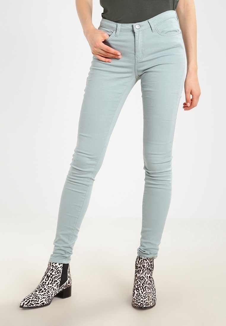 Personne portant un jean skinny bleu clair et des bottines à imprimé léopard noir et blanc, debout avec une main dans la poche.