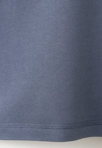 Gros plan sur un tissu gris avec une texture fine de tricot visible et un ourlet doublement cousu au bord inférieur d'un vêtement.