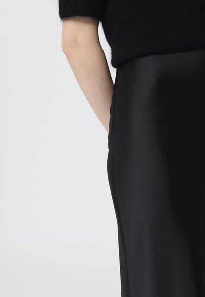 Zwarte satijnen rok met een gladde textuur, voorzien van een zijzak en een getailleerde pasvorm. Het kledingstuk is gecombineerd met een zwart fuzzy top.