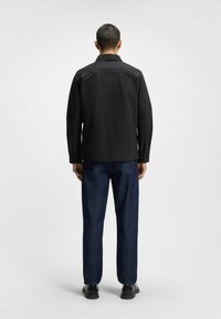 Sort langærmet skjorte med krave, glat tekstur, parret med mørke jeans og sorte sko. Enkel, funktionel design, ingen synlige mønstre.
