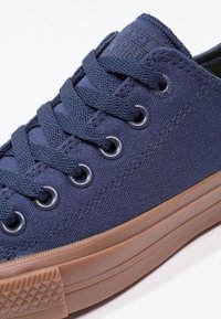Baskets en toile bleu marine avec lacets et œillets bleu foncé, semelle en caoutchouc beige et capuchon de orteil texturé, inclinées sur un fond blanc.
