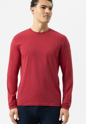 Rode longsleeve t-shirt van gladde stof. Beschikt over een ronde halslijn en een getailleerde pasvorm. Geëtaleerd op een model tegen een neutrale achtergrond.