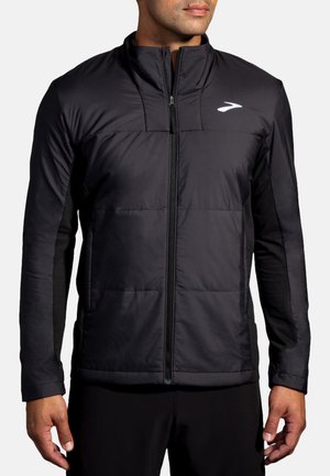 Schwarze Sportjacke mit Reißverschluss vorne, gesteppter Gestaltung am Oberkörper und glatten Seitenpanelen. Sie hat lange Ärmel und einen hohen Kragen.