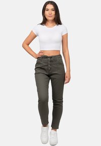 Olivgrüne, tapered Hosen mit einem Kordelzugbund, fünf Taschen und Knopfverschluss. Kombiniert mit einem taillierten, weißen T-Shirt mit kurzen Ärmeln und weißen Sneakers.