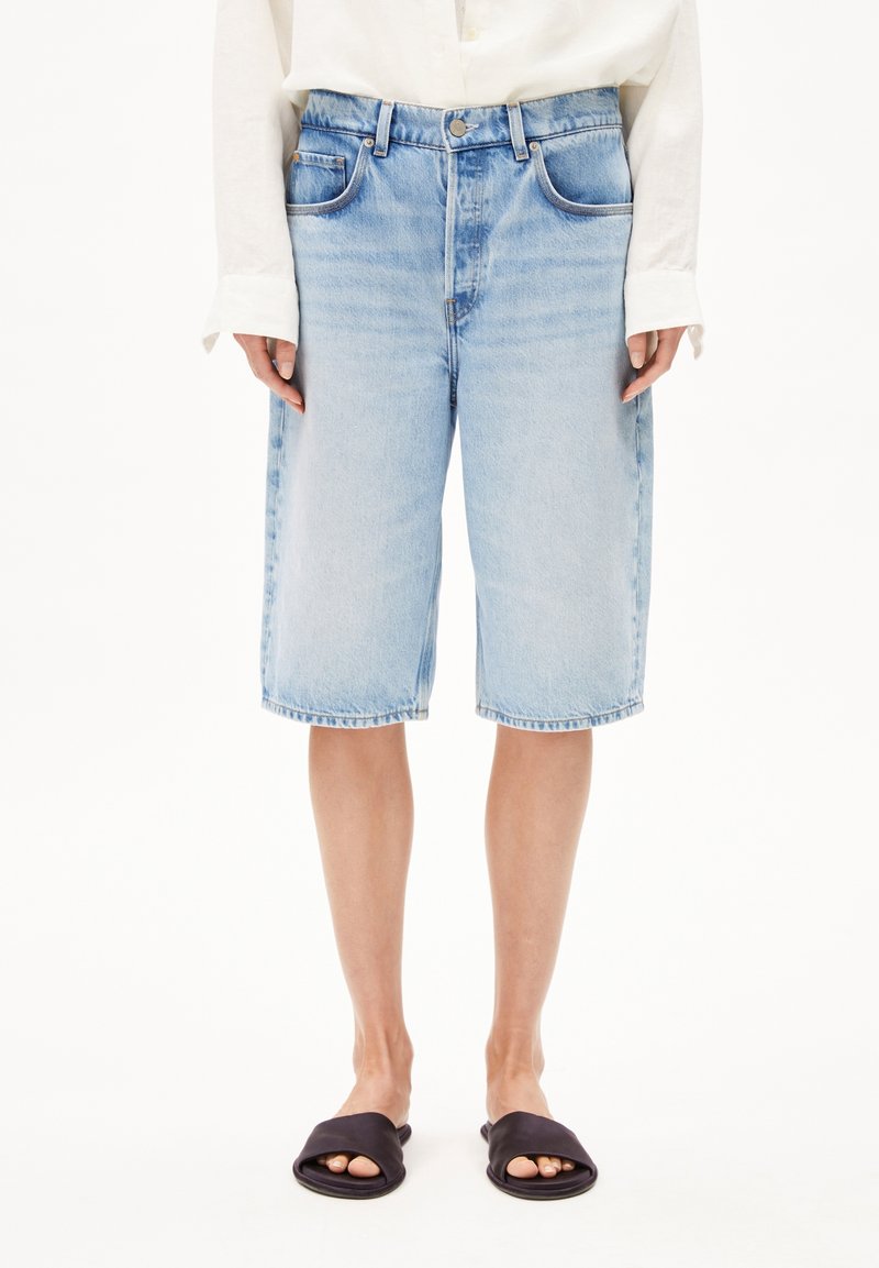 Vaaleansiniset rentomalliset farkkushortsit, joissa on viisi taskua, vyölenkit ja repsottava helma. Päällä mustat liukusandaalit.