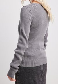 Harmaa, ribbineulottu pitkähihainen neulepaita, jossa on istuva malli, pyöreä pääntie ja teksturoitu kangas, joka tarjoaa sileän pinnan ja tiukan istuvuuden.