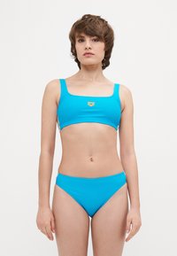 Šviesiai mėlynas dviejų dalių bikini, pagamintas iš lygaus, tamprumo turinčio audinio. Viršus su kvadratiniu iškirpimu, plonomis petnešėlėmis ir derančiomis aukštu liemeniu kelnaitėmis.