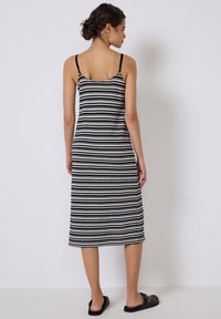 Schwarz-weiß gestreiftes Midikleid mit Spaghettiträgern, taillierten Silhouette und strukturierter Strickware. Getragen mit schwarzen Riemensandalen.