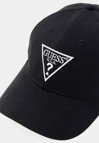 Schwarze Stoffmütze mit einem dreieckigen, weißen, gestickten Logo, das "GUESS USA" und ein Fragezeichen zeigt. Strukturiertes Design und gebogener Schirm.
