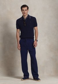 Jūrinis polo marškinėliai trumpomis rankovėmis su baltais akcentais, derinami su tamsiai mėlynomis stringinėmis kelnėmis ir espadrilėmis. Švarus, modernus įvaizdis.