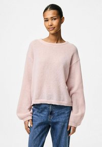 Ljusrosa stickad tröja med rund halsringning och lösa, långa ärmar. Tröjan har en texturerad yta och en kortad nederkant. I kombination med blå jeans.