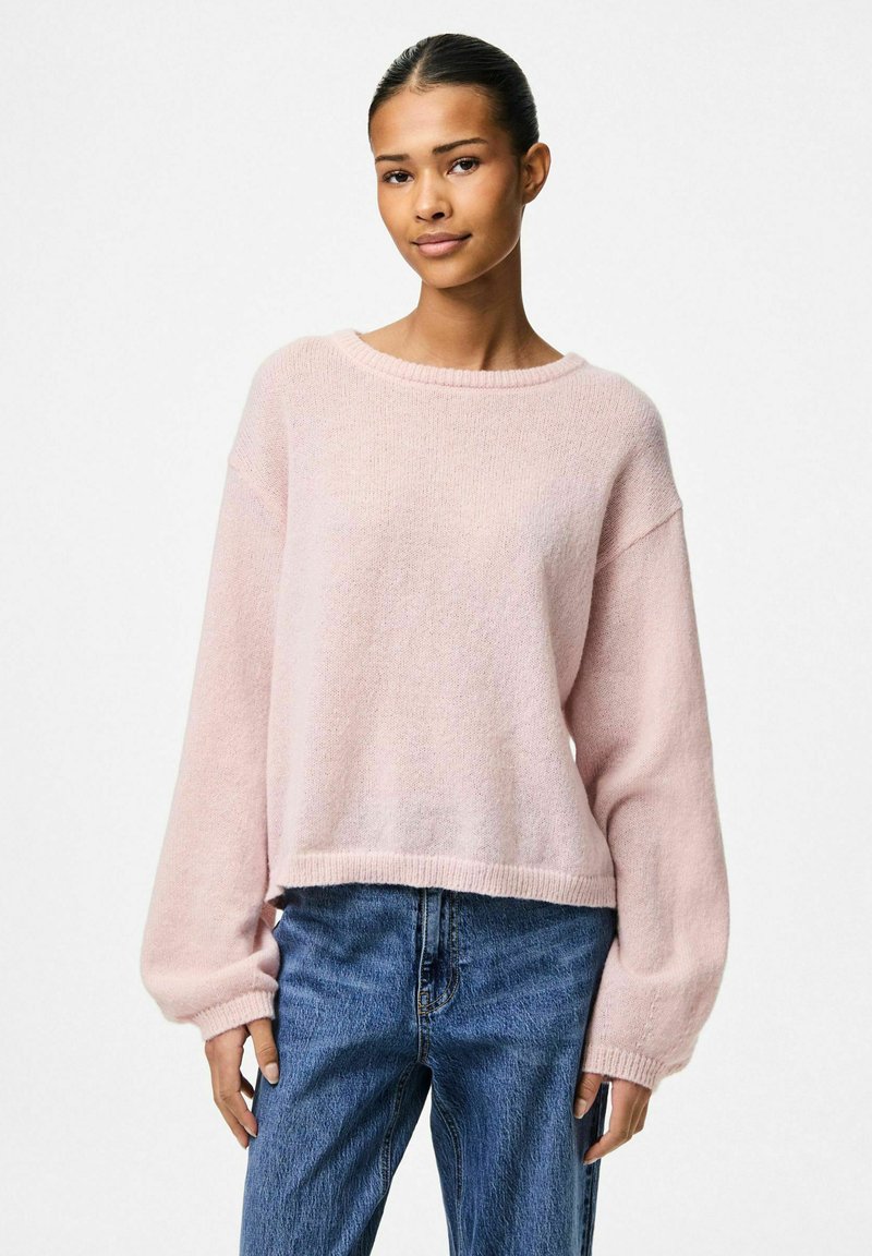 Ljusrosa stickad tröja med rund halsringning och lösa, långa ärmar. Tröjan har en texturerad yta och en kortad nederkant. I kombination med blå jeans.