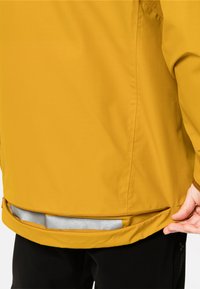Gelbe wasserdichte Jacke mit strukturiertem Oberflächenmaterial, einem Reißverschluss am Saum und verstellbarem Schnitt. Sie zeichnet sich durch ein schlankes Design und minimale Hardware aus.