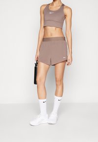 Bruine sportieve crop top en bijpassende shorts met een Nike-logo. Witte sokken en schoenen complementeren de outfit, die een sportief ontwerp heeft.