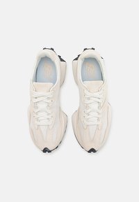 Un paio di sneakers bianche e beige della New Balance con lacci, viste dall'alto su uno sfondo bianco uniforme.