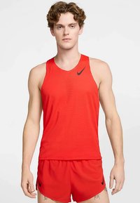 Joven con una camiseta sin mangas roja de Nike y pantalones cortos a juego, de pie contra un fondo blanco liso.