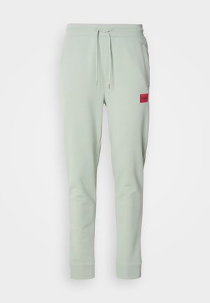 Pantaloni della tuta verde chiaro con vita elastica e cordoncino. Presentano un'etichetta rossa sulla coscia sinistra. Polsini alle caviglie. Materiale in misto cotone.