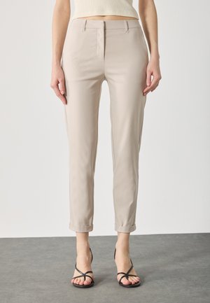 Lys beige bukser med en glat tekstur, tætsiddende pasform og opbrettede manchetter. Sammen med sorte sandaler med stropper.