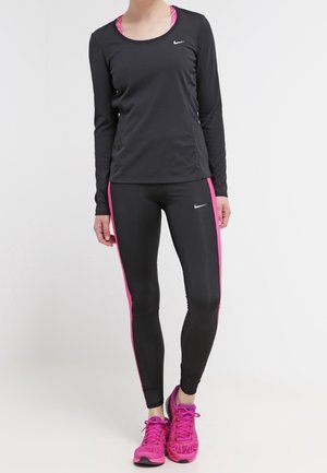 Haut de sport à manches longues noir associé à un legging noir avec des rayures latérales roses et des chaussures de sport rose vif. Marque Nike visible.