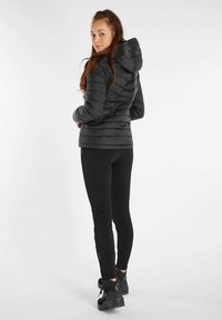 Zwarte pufferjack met een capuchon en gewatteerde delen. Zwarte leggings en stevige zwarte wandelschoenen maken de outfit compleet.
