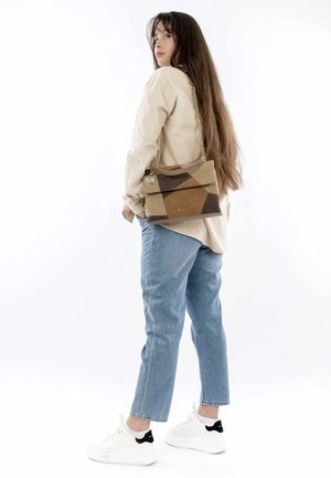 Tan and brown leather handbag with a geometric design, featuring a chain strap and a logo detail, worn over a beige shirt and light jeans.