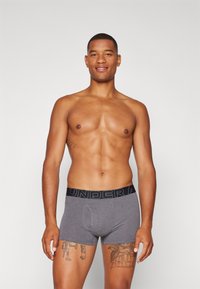 Szürke boxer alsónadrág fekete gumírozott derékrésszel, amelyen a "UNDER ARMOUR" felirat szerepel. Az anyag simának, ruganyósnak és feszesnek tűnik.