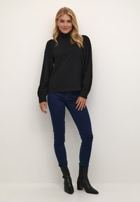 Černé texturované tričko s dlouhým rukávem a vysokým límcem, v kombinaci s tmavě modrými skinny džíny a černými špičatými kotníkovými botami. Celkově jednoduchý design.