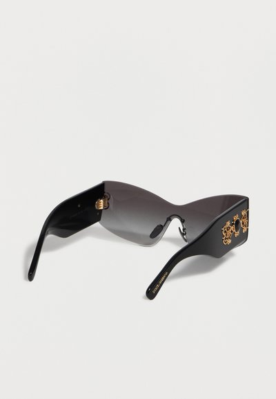 Lunettes de soleil bouclier noires surdimensionnées avec des verres dégradés et des détails ornementaux dorés sur les branches épaisses.