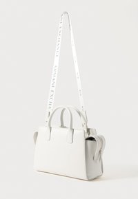 Bolsa branca em pele sintética com um formato estruturado, alças duplas na parte superior, bolso lateral com fecho e uma alça destacável com impressão do logotipo.