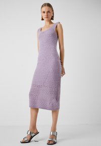 Abito lavorato a maglia lilla con silhouette aderente, spalline larghe e un intricato motivo in pizzo. Abbinato a sandali con tacco argentati dotati di una fibbia.