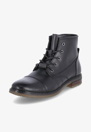Bottine noire en cuir avec un bout rond, fermeture à lacets, œillets en métal et semelle brune contrastante. Présente des détails de couture visibles.