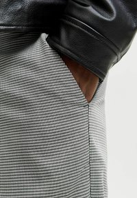 Mustmust nahkjakki vars, mis on läheduses halli ja valgega kootud ruudulise mustriga pükste. Kangas on tekstuuriga ja omab õrna sära.