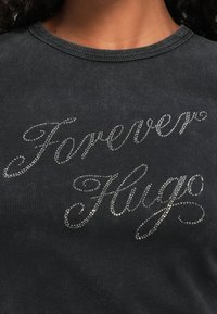 Donkergrijze corduroy overhemd met de tekst "Forever Hugs" in zilveren rhinestones, prominent weergegeven op de borst.