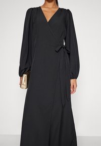 Svarts wrap-klänning i lätt tyg, med långa ärmar, djup V-ringning och detaljer med knytning på sidan. Slen textur med minimal design.
