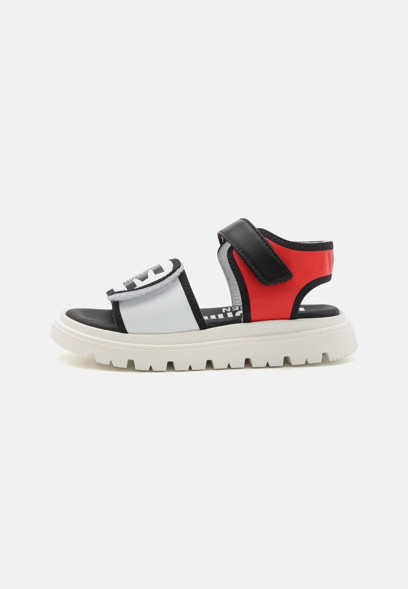 Sandal colorido con un diseño en blanco, negro y rojo, con una suela gruesa blanca, correas ajustables y una parte superior texturizada.