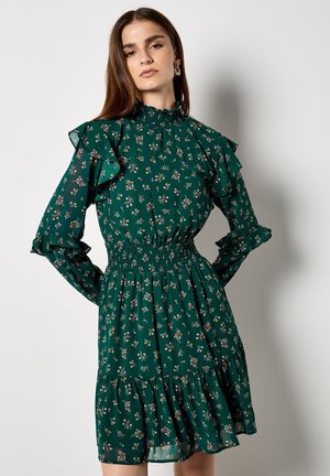 Abito floreale verde con lunghe maniche a rouches e vita smerlata. Presenta una gonna a strati con piccoli motivi floreali su tutta la superficie.