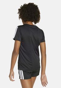 Maglietta atletica nera a maniche corte, con strisce bianche sulle spalle, abbinata a pantaloni corti neri, che mostrano una texture liscia.