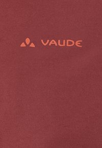 Raudonas audinys su lygiu paviršiumi, ant kurio yra oranžinė "VAUDE" logotipo forma ir trikampis akcentas viršuje. Paprastas dizainas, be raštų.
