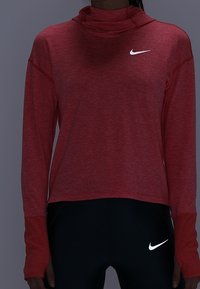 Hoodie rosso a maniche lunghe realizzato in tessuto morbido con colletto alto. Presenta un logo Nike bianco sul petto e pantaloni neri a contrasto.