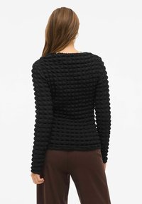 Maglietta nera a maniche lunghe con texture, motivo a griglia e scollatura tonda, design affusolato e polsini a costine, abbinata a pantaloni marroni.