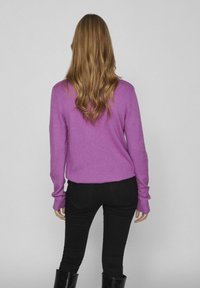 Pull violet en tissu doux, avec une coupe décontractée et des manches longues, associé à un pantalon noir ajusté et des bottes. Vue de dos.