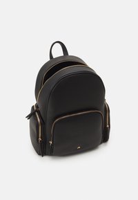 Svart läderryggsäck med texturerad yta, två framfickor med blixtlås och guldhardware-accenter. Rundad form och topphandtag för bärande.