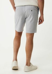 Helleblaue gestreifte Shorts mit flachem Bund, seitlichen Taschen und einer geknöpften Gesäßtasche. Getragen mit weißen Turnschuhen.