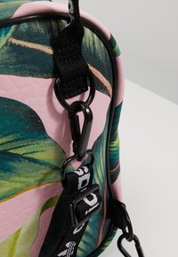 Zielony wzór liści na różowym tle, z czarnymi elementami metalowymi, teksturowaną powierzchnią oraz regulowanymi paskami zapewniającymi różnorodne opcje noszenia.